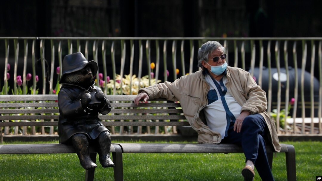 A man relaxes on a bench in London, next to a sculpture of Paddington Bear, as the country is in lockdown to help curb the spread of the coronavirus, April 15, 2020.