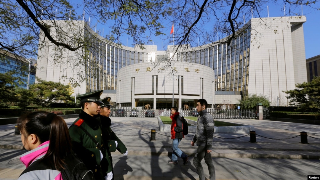 FILE - People walk past the headquarters of the People's Bank of China as two police officials patrol the area in Beijing Nov. 20, 2013. 