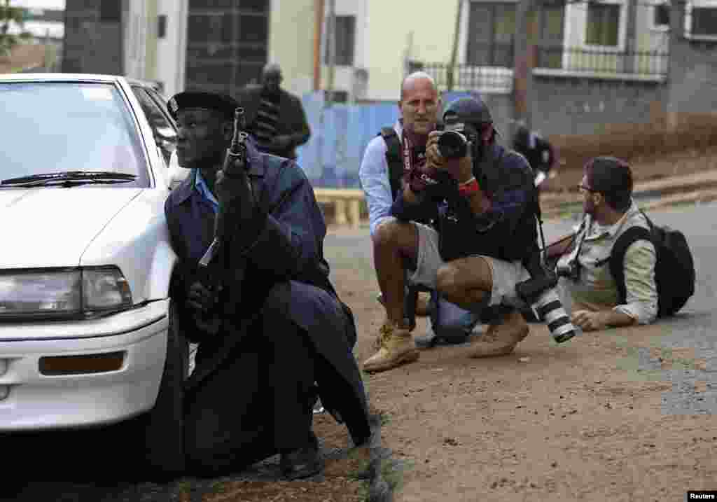 A policeman and photographers take cover after hearing gun shots near the Westgate shopping center in Nairobi, Kenya, Sept. 23, 2013.