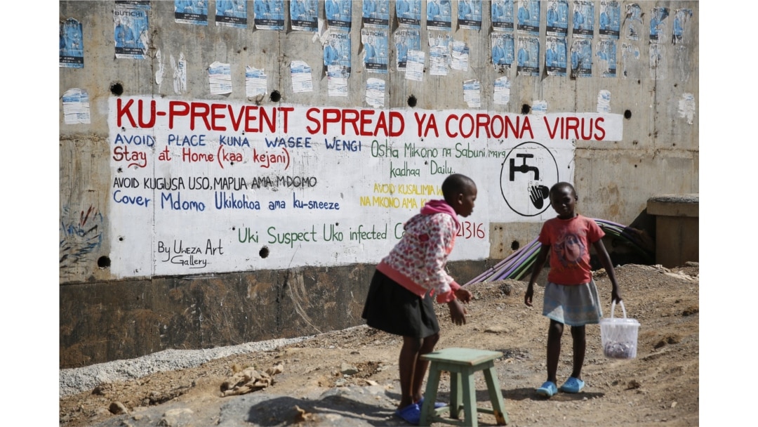 Two young girls sell groundnuts in front of an informational mural advising on precautions to avoid catching the new coronavirus, in the Kibera slum, or informal settlement, of Nairobi, Kenya Thursday, April 2, 2020.