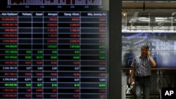 FILE - A man speaks his on his cellphone next to an index board at the reception hall of the Stock Exchange in Athens, July 25, 2017. 