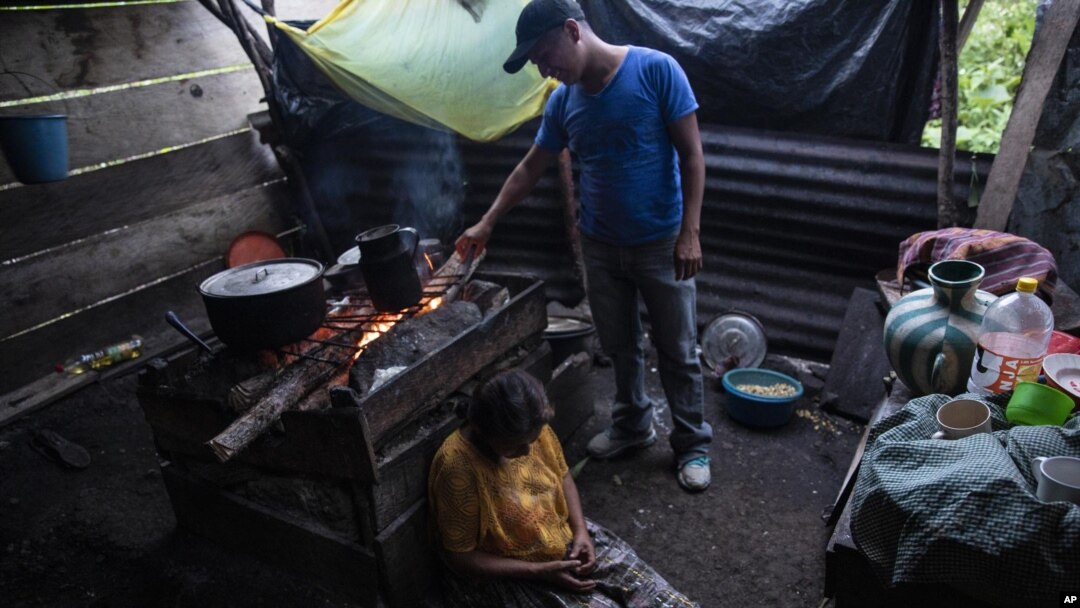 Pascuala Jonaj sits against a wood-burning stove as her son Victor Cal feeds the fire a day before he begins his trip to the United States, inside their home at the makeshift settlement Nuevo Queja, Guatemala, Thurs., July 8, 2021. (AP Photo/Rodrigo Abd)