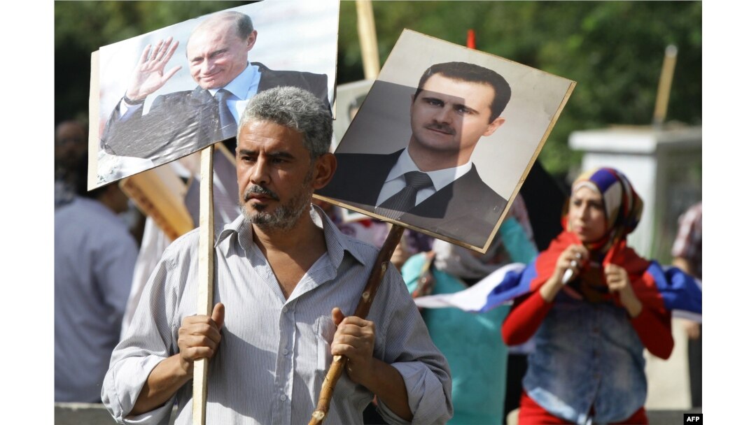 A Syrian man holds portraits of President Bashar al-Assad, right, and Russian President Valdimir Putin, left, as several hundred people gathered near the Russian Embassy in Damascus to express their support for Moscow's air war in Syria.
