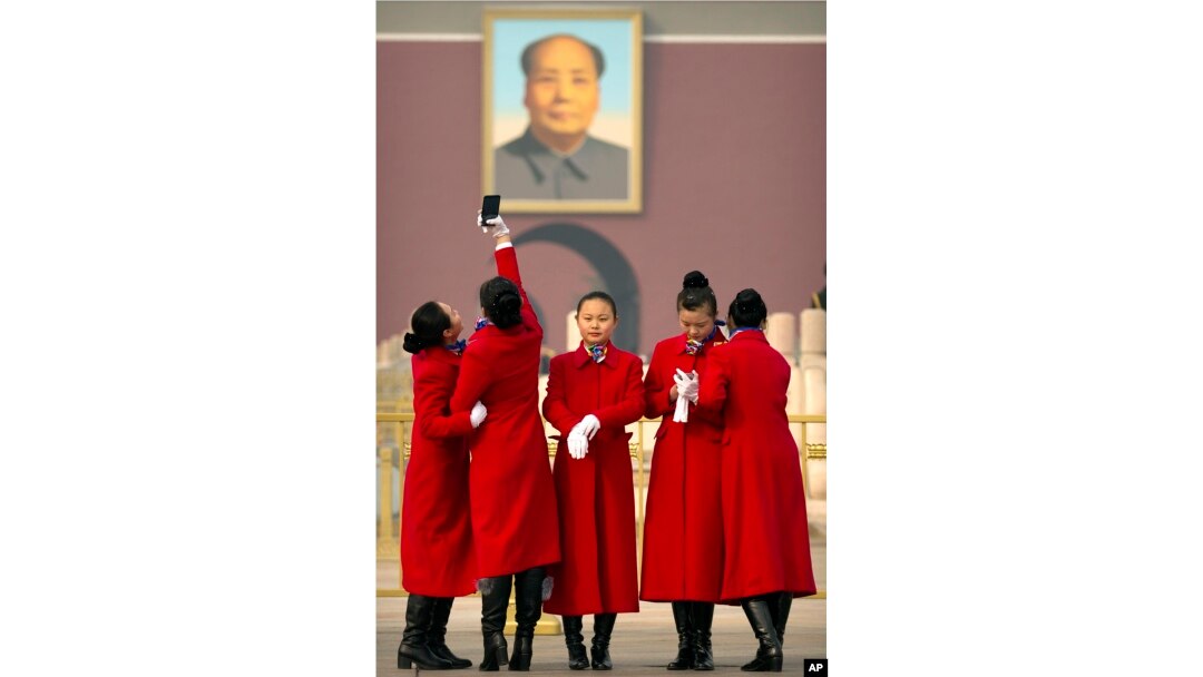 Hospitality staff members pose for a selfie near the portrait of Chinese leader Mao Zedong during the opening session of the Chinese People's Political Consultative Conference (CPPCC) held in Beijing's Great Hall of the People, Saturday, March 3, 2018. (A