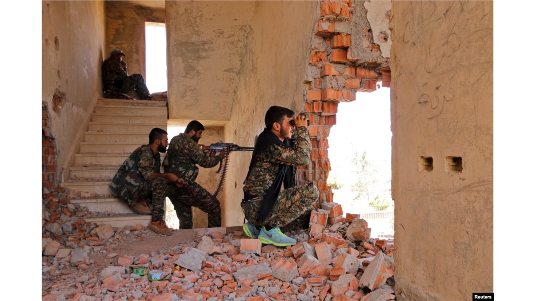 FILE - Kurdish People's Protection Units (YPG) fighters take up positions inside a damaged building in al-Vilat al-Homor neighborhood in Hasaka city, as they monitor the movements of Islamic State fighters stationed in Ghwayran neighborhood.
