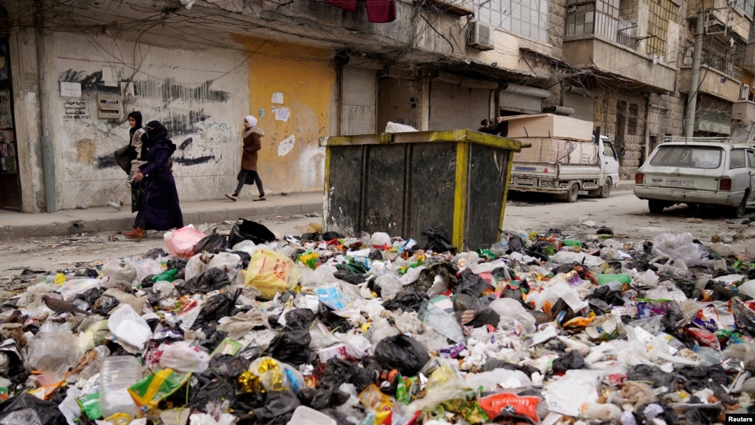 Women walk past piled up garbage after rebels took the main northern city of Aleppo and have since pushed south from their enclave in northwest Syria, Dec. 4, 2024.