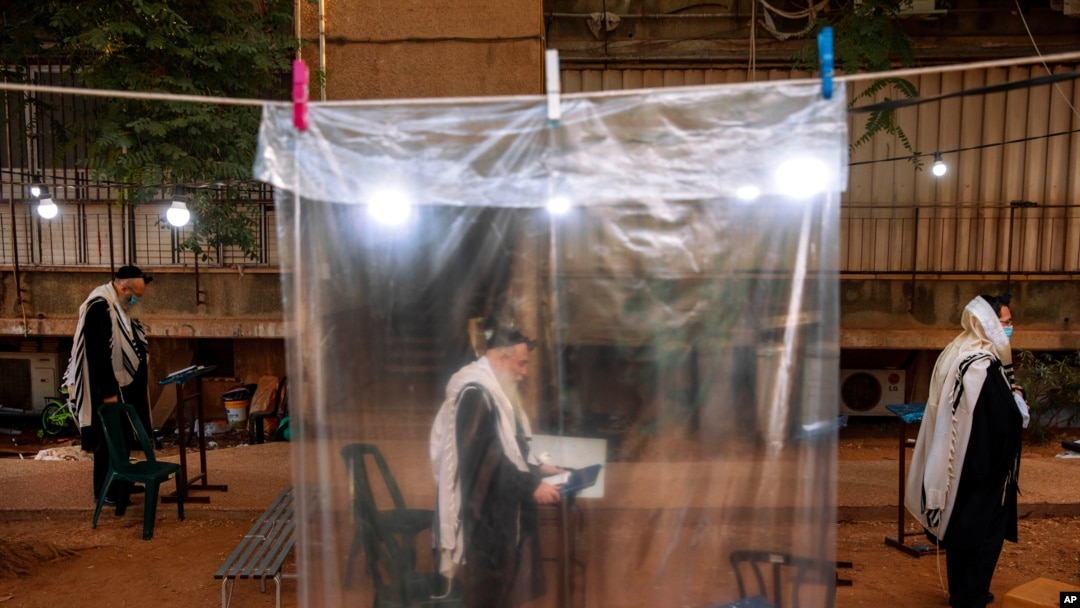 Ultra-Orthodox Jews keep social distancing and wear face masks during a morning prayer next to their houses as synagogues are limited to twenty people following the government's measures to help stop the spread of the coronavirus, in Bnei Brak, Israel.