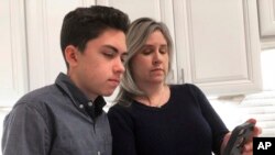 FILE- Grant Thompson and his mother, Michele, look at an iPhone in the family's kitchen in Tucson, Ariz., Jan. 31, 2019. Apple has released an iPhone update to fix a FaceTime flaw that Grant was credited with spotting.
