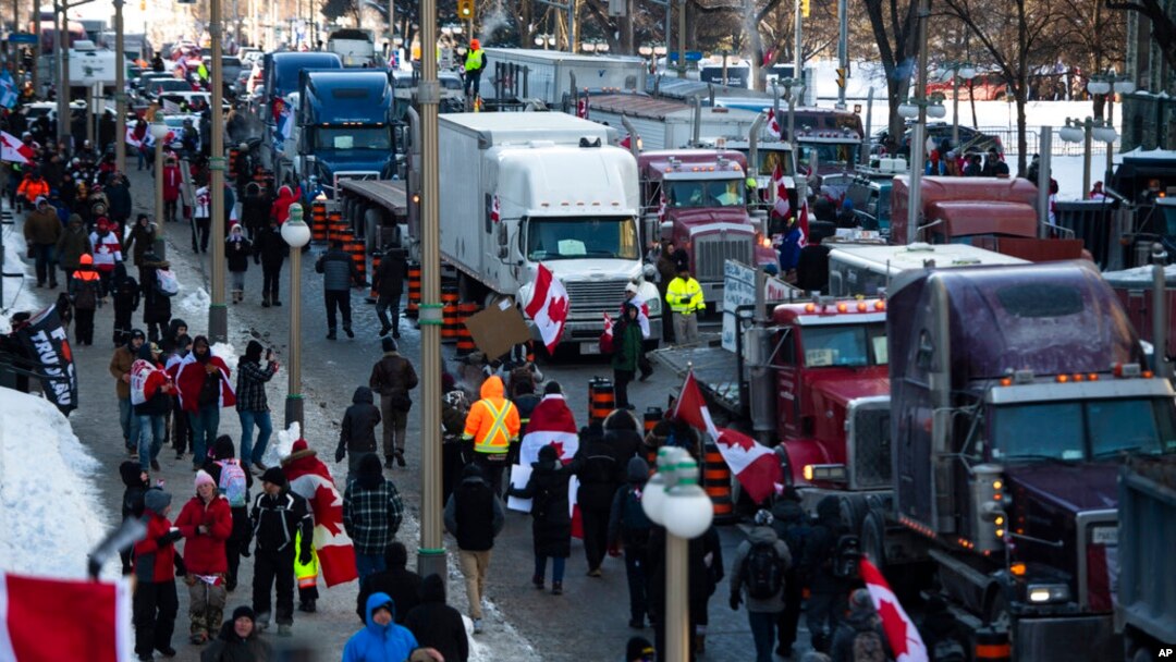 FILE - People walk past parked trucks on Wellington Street during a demonstration against COVID-19 restrictions at Parliament House in Ottawa, Canada, on Jan. 29, 2022.