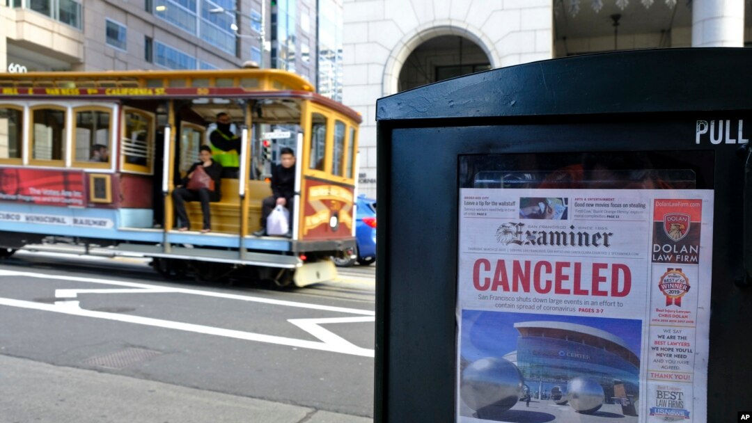 A newspaper headline announcing the closure of large events is displayed as a cable car goes down California Street in San Francisco. 