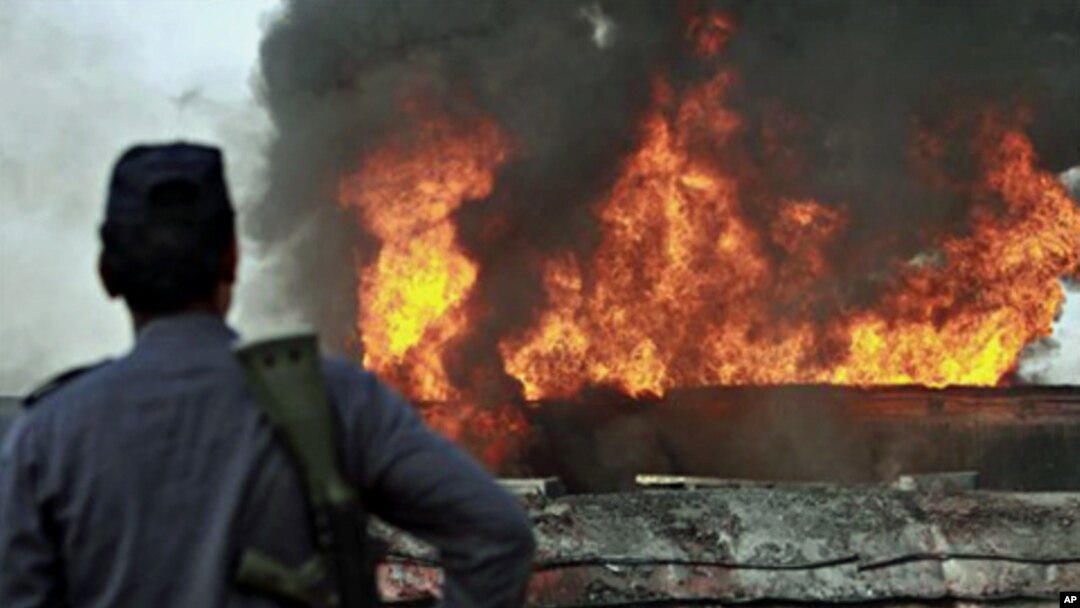Pakistani police officer stands guard on still smoldering oil trucks in Shikarpur, southern Pakistan, 01 Oct. 2010