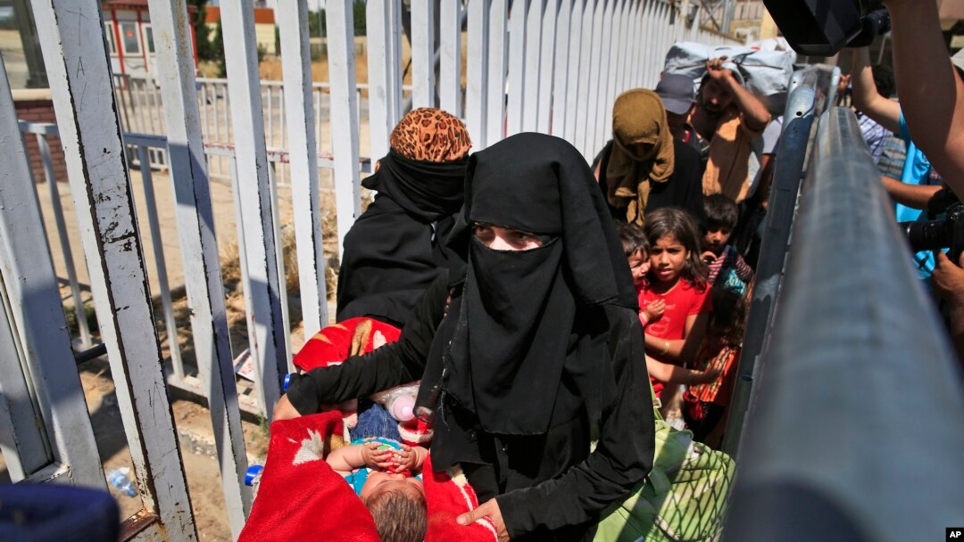 FILE - A Syrian woman caring a baby, walks with others to cross back to the border town of Tal Abyad in Syria from Turkey, at the border crossing in Akcakale, southeastern Turkey, June 17, 2015. 