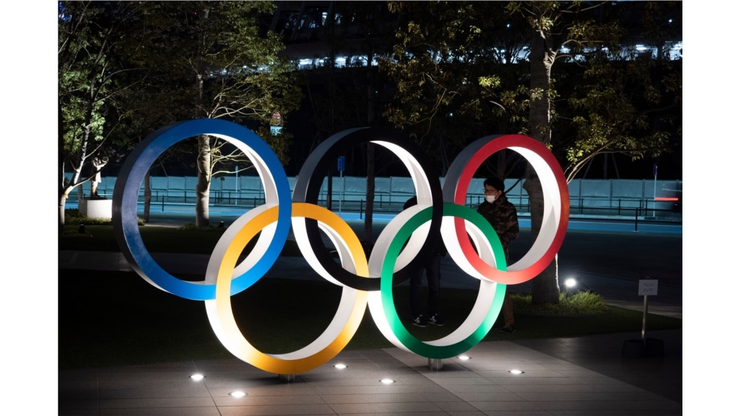 Two men chat behind the Olympic rings near the New National Stadium in Tokyo, March 24, 2020.