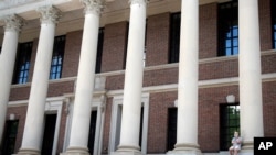 FILE - A man wearing a face mask to protect against the coronavirus talks on his phone on the steps of Harvard University's Widener Library, in Cambridge, Massachusetts, June 26, 2020.