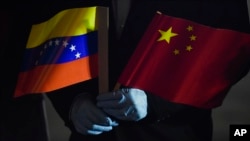FILE - Venezuelan Foreign Minister Jorge Arreaza, wearing protective gloves as a preventive measure against the spread of COVID-19, holds Venezuelan and Chinese flags at the Simon Bolivar International Airport in La Guaira, Venezuela, on March 30, 2020.