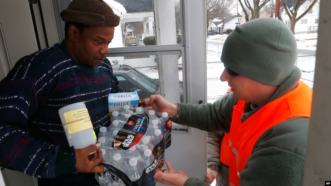 FILE - Michigan National Guard specialist Joe Weaver, right, delivers clean water supplies to Louis Singleton and other residents of Flint, Jan. 21, 2016.