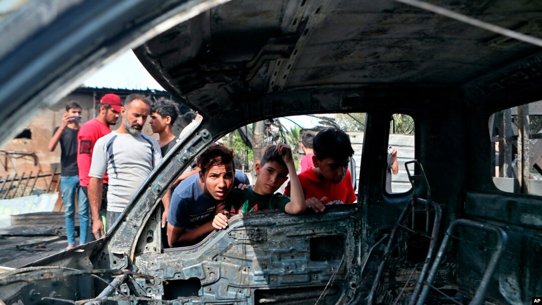 Boy look at a damaged vehicle at the scene of a powerful explosion at a crowded outdoor used furniture market in Sadr City neighborhood of Baghdad, Iraq, April 15, 2021.