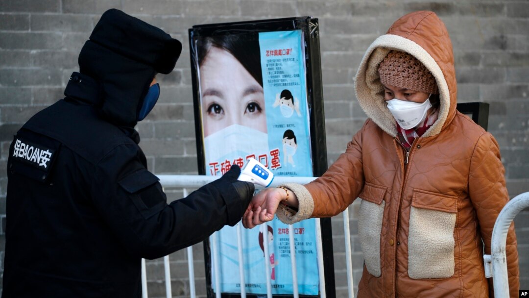 A woman wearing a protective face mask receives a temperature check from a security guard as she enters Qianmen Street, a popular tourist spot, in Beijing, Feb. 16, 2020. 