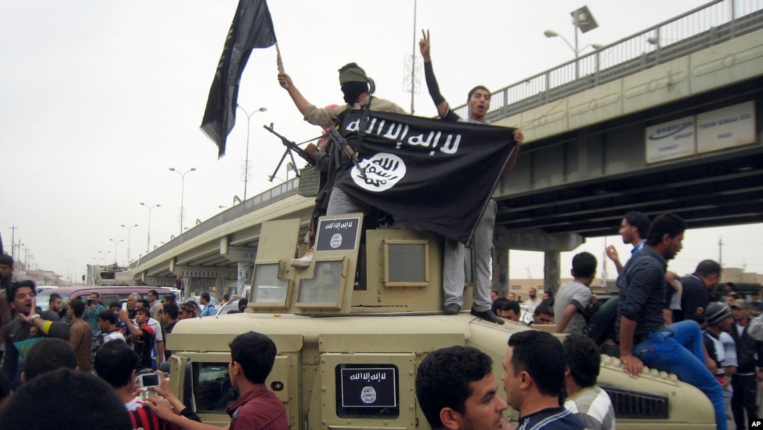 FILE - Islamic State group militants hold up their flag as they patrol in a commandeered Iraqi military vehicle in Fallujah, Iraq, March 30, 2014. 
