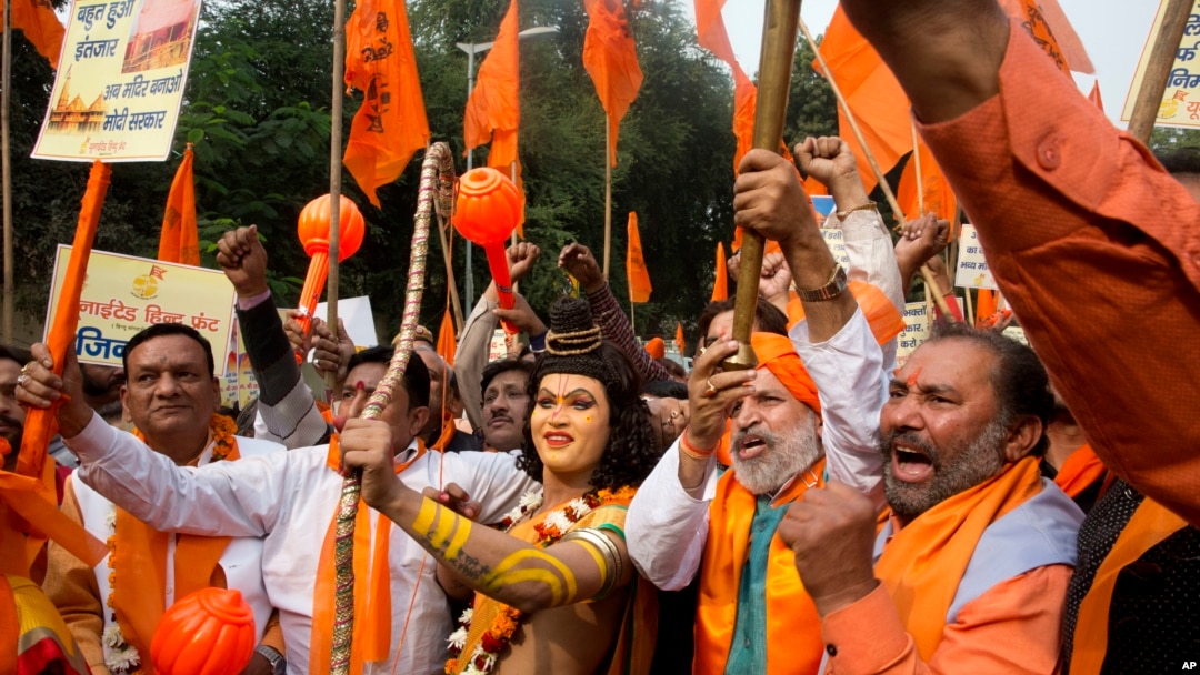 FILE - A man stands dressed as Hindu god Ram, center, as activists of right wing Hindu groups shout slogans demanding that a temple of Hindu god Ram be made at Ayodhya on the anniversary of the Babari Mosque demolition in New Delhi, India, Dec. 6, 2018. 