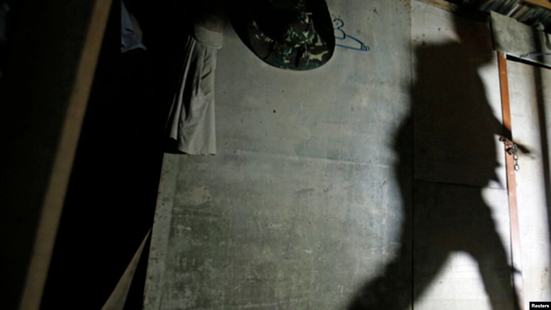 A shadow of a migrant enforcement officer is cast on a makeshift shelter, built by suspected illegal migrant workers, as he tries to break a locked door during a crackdown on illegal migrant workers in Nilai, outside Kuala Lumpur September 1, 2013. 