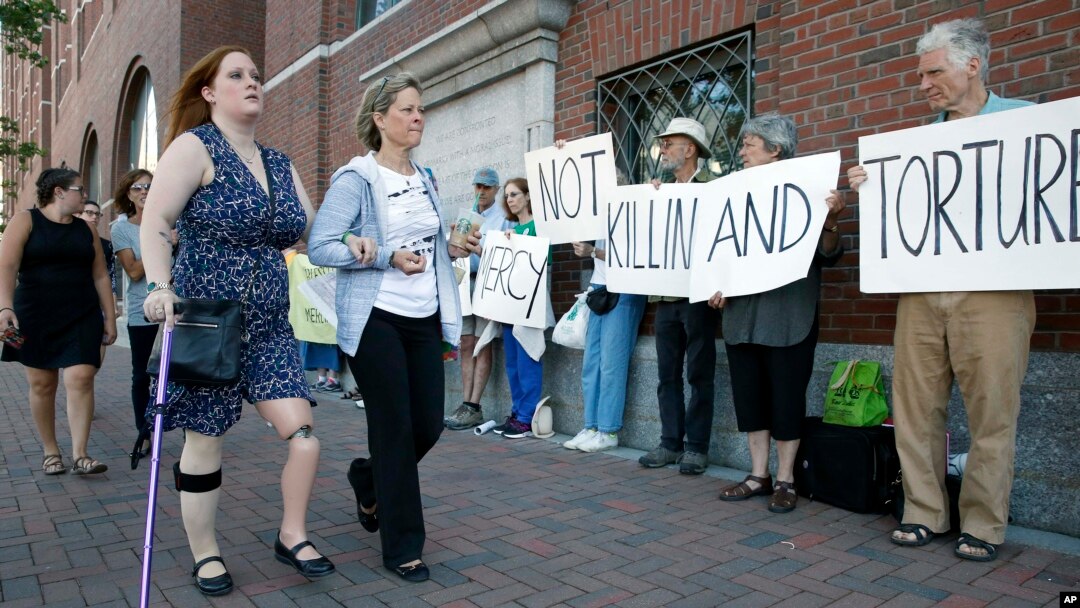Boston Marathon bombing victim Erika Brannock, foreground left, and her mother, Carol Downing, foreground right, walk past demonstrators outside federal court in Boston, June 24, 2015.