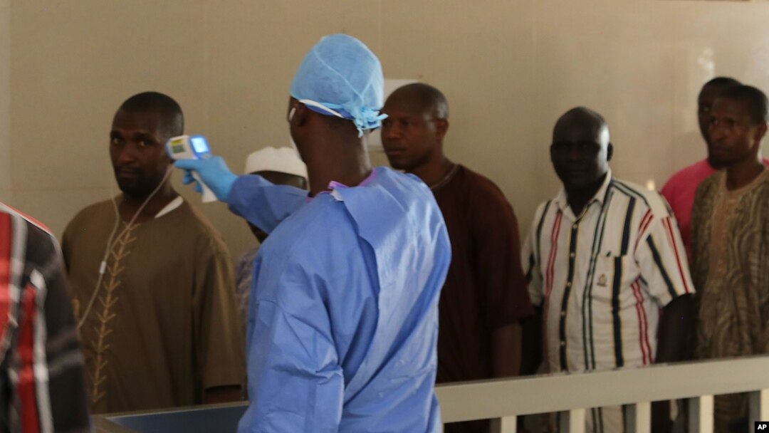 A health worker, center, takes the temperature of people to see if they might be infected by the Ebola virus inside the Ignace Deen government hospital in Conakry, Guinea, March 18, 2016.