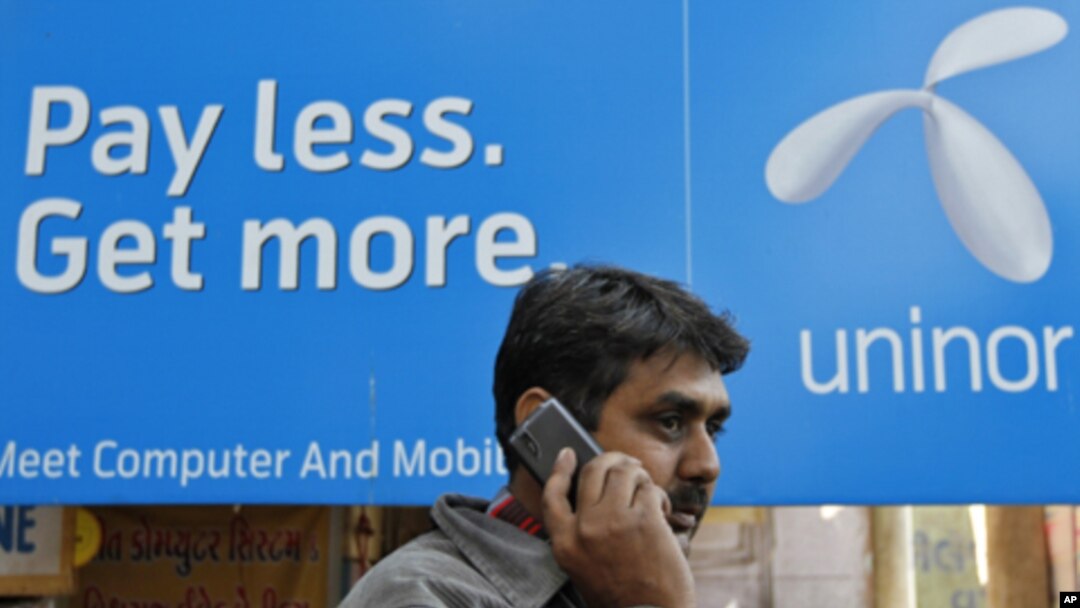 A man speaks on a mobile phone in front of a billboard of Uninor at a market in Ahmedabad, February 6, 2012. Telenor's joint venture with Unitech, which operates under the Uninor brand, has been among the most aggressive of India's newer telecoms compani