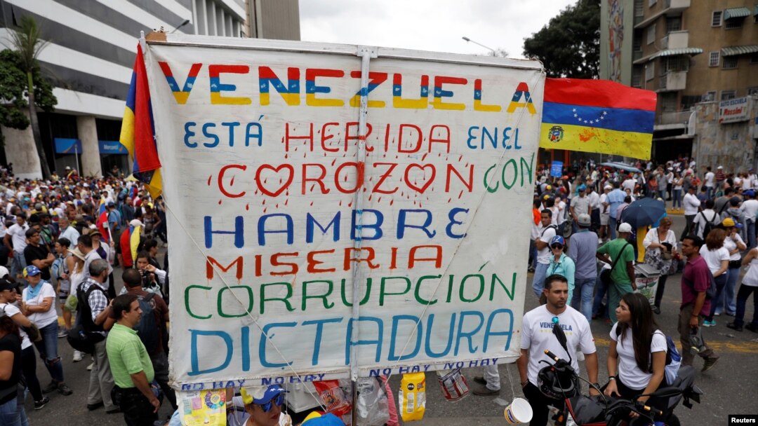 ARCHIVO - Simpatizantes de la oposición protestan contra el presidente Nicolás Maduro con un cartel que dice "Venezuela está herida en el corazón con hambre, miseria, corrupción y dictadura", en Caracas, Venezuela, el 10 de mayo de 2017.
