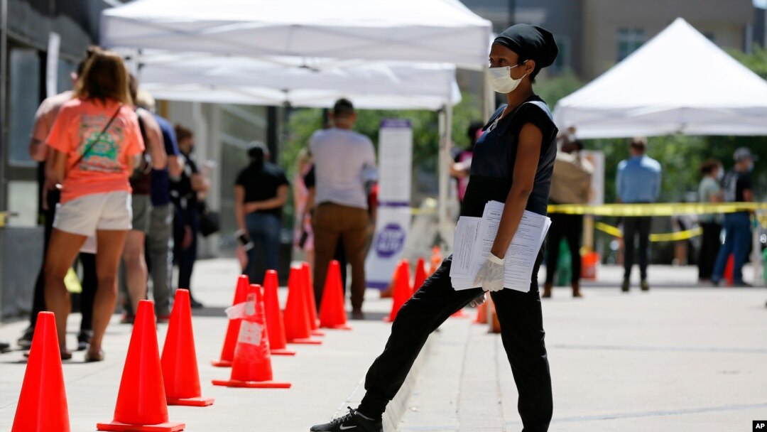 FILE - A medical assistant, right, provides paperwork to people in line at a walk-up COVID-19 testing site in Dallas, Texas, June 11, 2020.