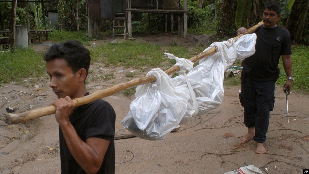 Workers carry a dead body in Songkhla province, southern Thailand, May 1, 2015. Police in Thailand found dozens of shallow graves Friday and at least one corpse in an isolated mountain shelter that is believed to be a trafficking camp for ethnic Rohingya Muslims fleeing Myanmar.
