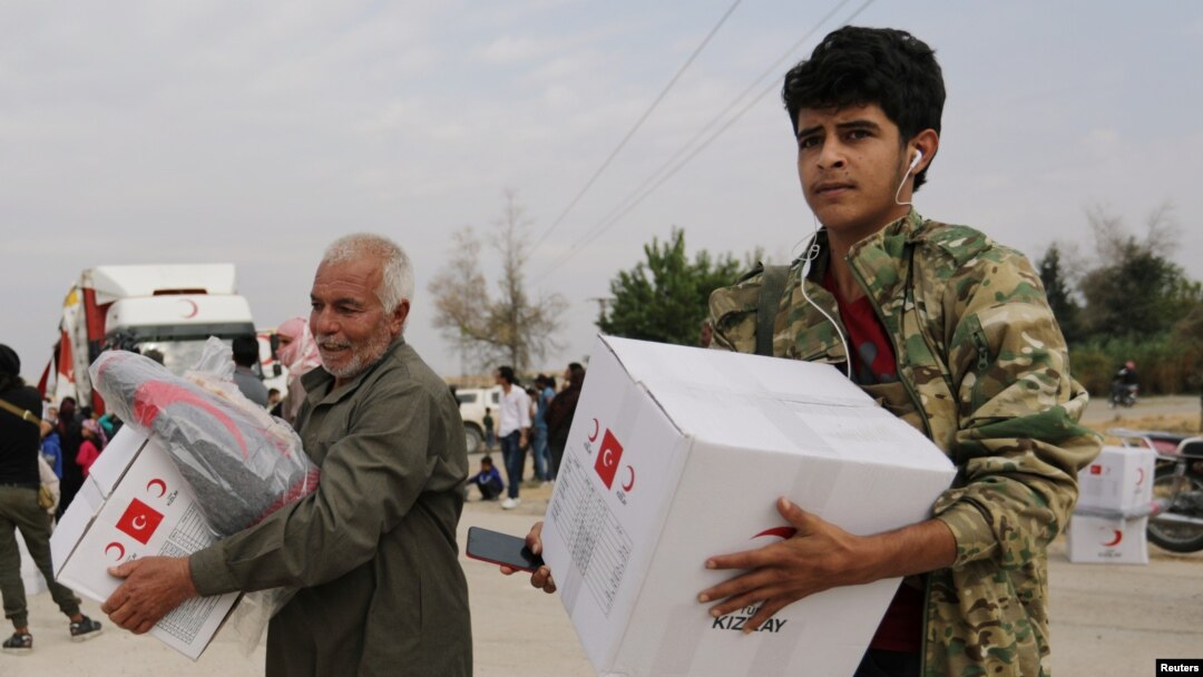FILE - People hold boxes of aid donated by the Turkish Red Crescent in the border town of Tal Abyad, Syria, Oct. 19, 2019.