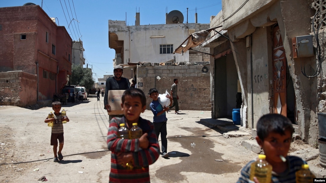 FILE - Syrian children and a man are seen carrying food aid in Douma, near Damascus, Syria, Aug. 6, 2017.