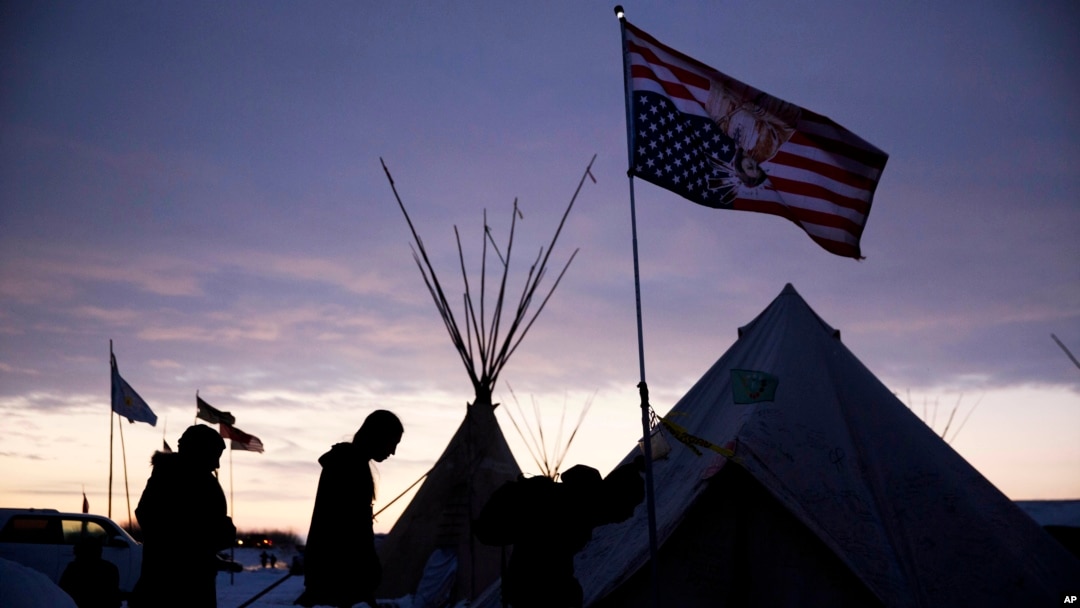 FILE - In this Dec. 2, 2016, file photo, travelers arrive at the Oceti Sakowin camp where people have gathered to protest the Dakota Access oil pipeline as they walk into a tent next to an upside-down american flag in Cannon Ball, N.D.